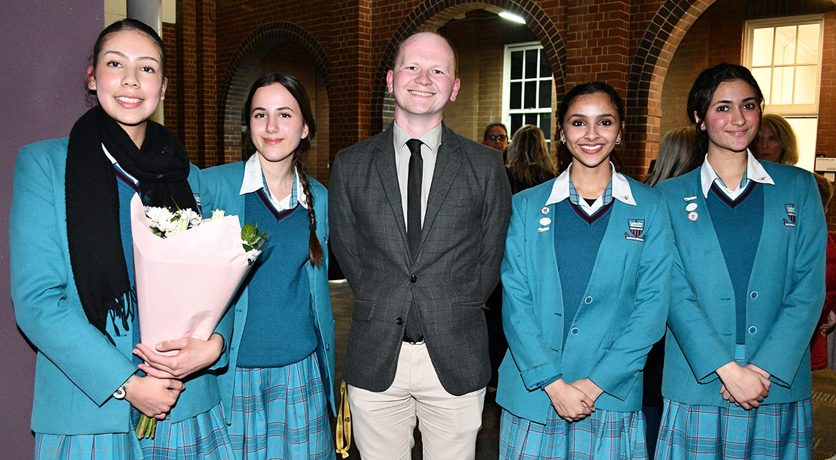 Catherine McAuley Westmead students posing for a photo with Mr Thomas Fraser. One student is holding flowers.