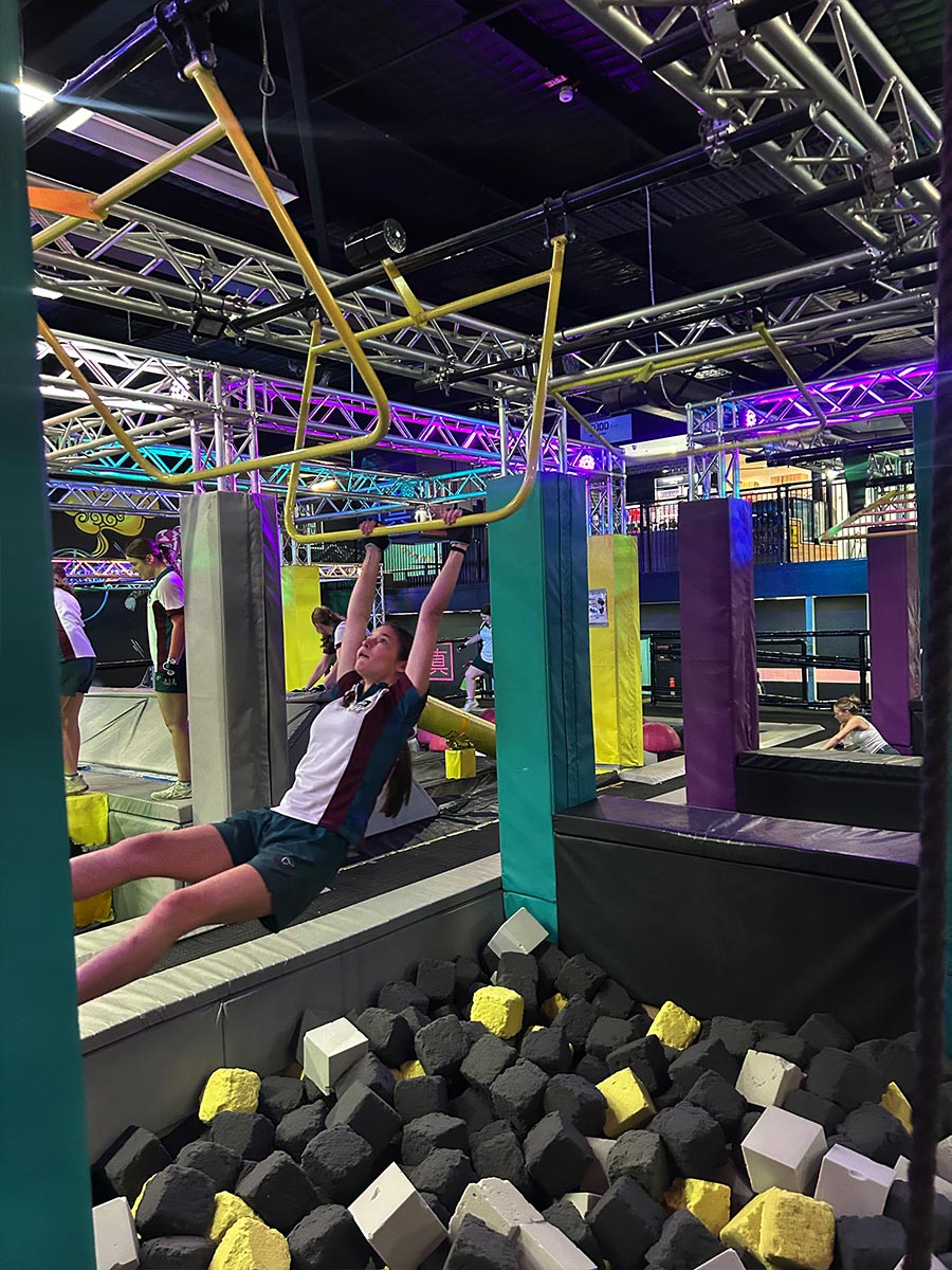 Catherine McAuley Westmead student swinging above a pit of foam cubes at Tru Ninja Warrior