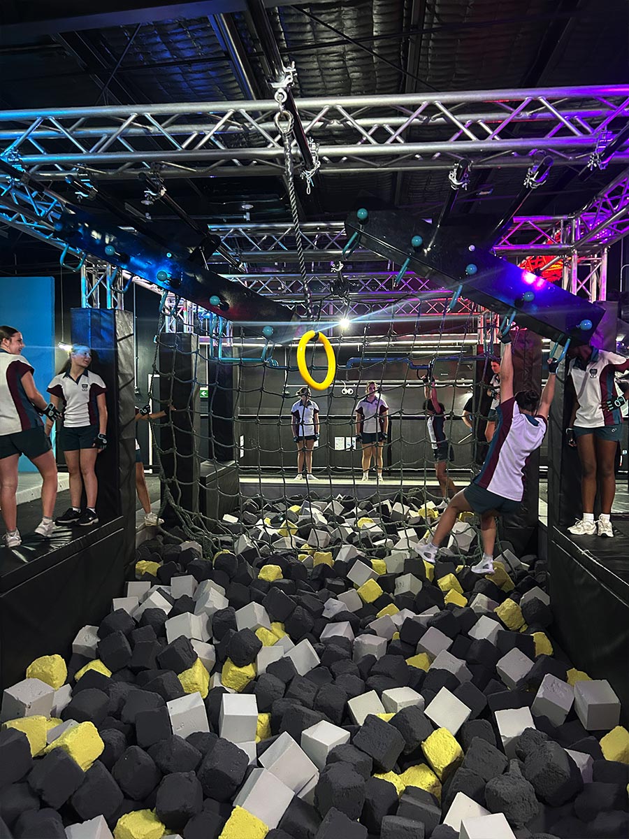 Catherine McAuley Westmead student swinging above a pit of foam cubes at Tru Ninja Warrior
