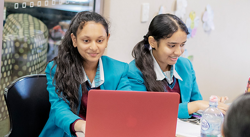 Two smiiling Catherine McAuley Catholic College Westmead who are using MacBooks