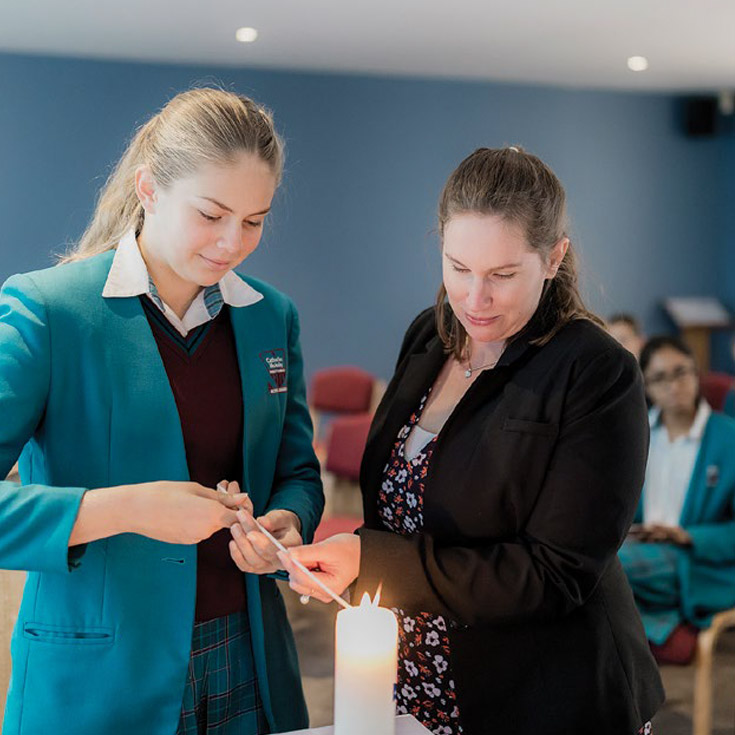 Liturgy at Catherine McAuley Catholic College Westmead. One student and a teacher are lighting a candle.